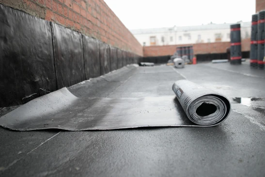 Chantier de construction extérieur avec ouvrier déroulant membrane d'étanchéité bitumineuse sur toiture-terrasse